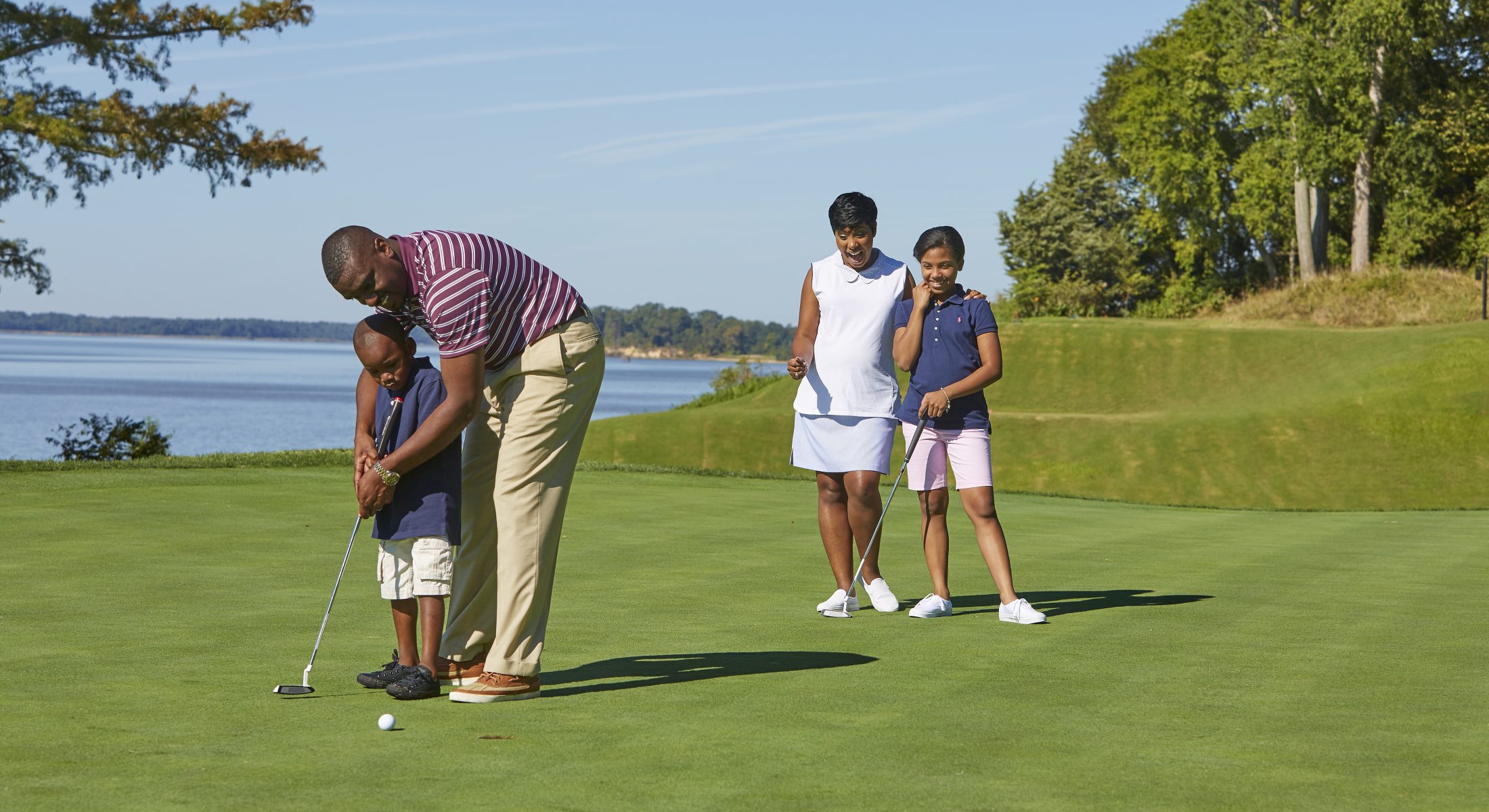 Father Teaching Son to Golf With Mother and Daughter Watching